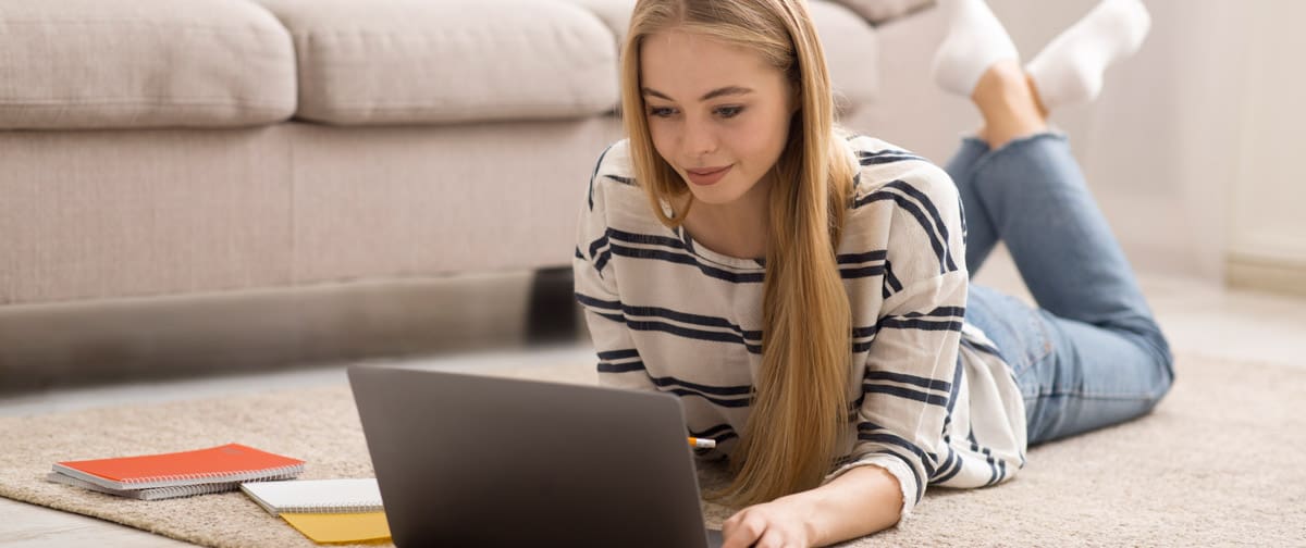 Blonde girl student studying at home, laying on floor